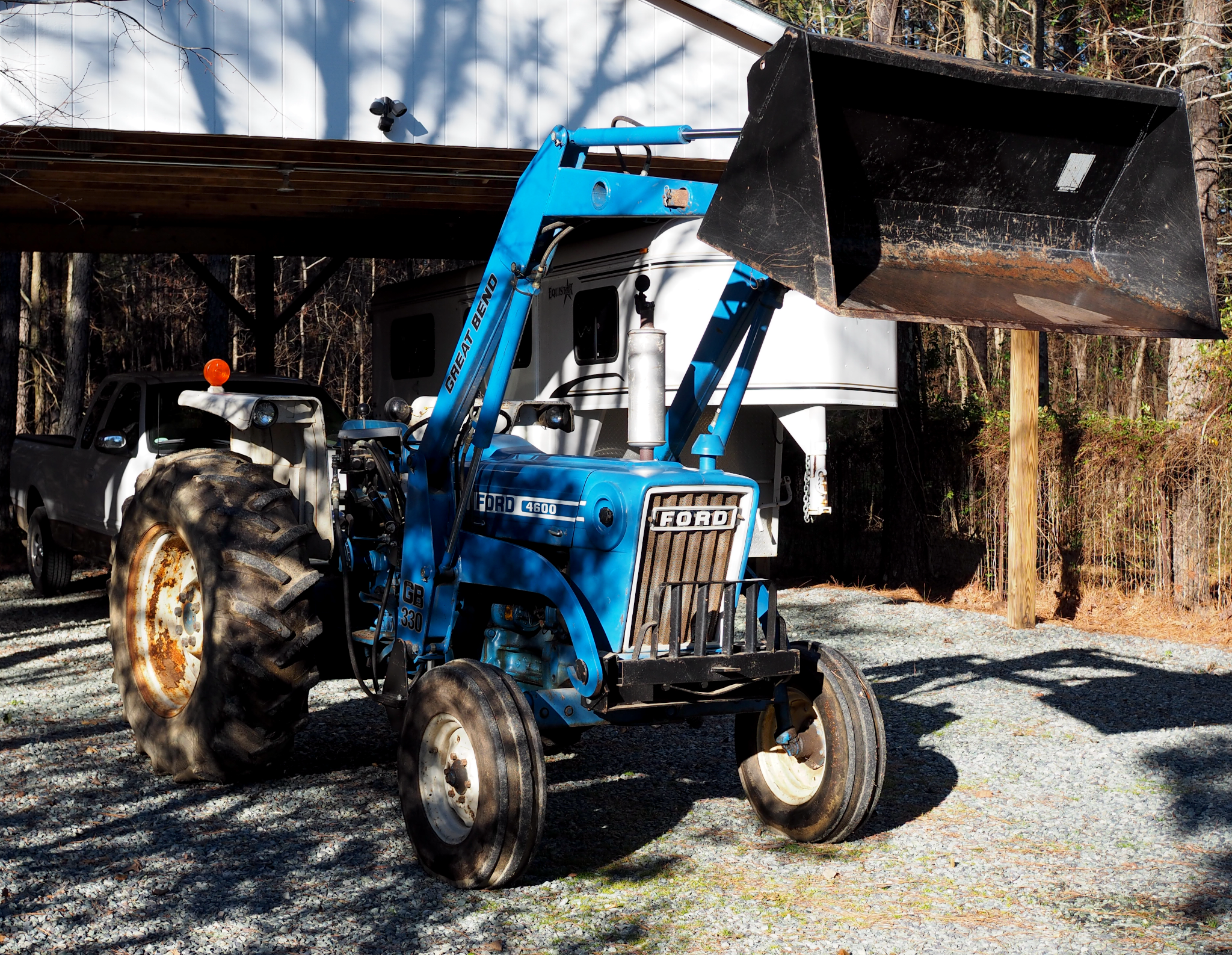 A blue Ford 4600 tractor with white rims and a front end loader raised in the air