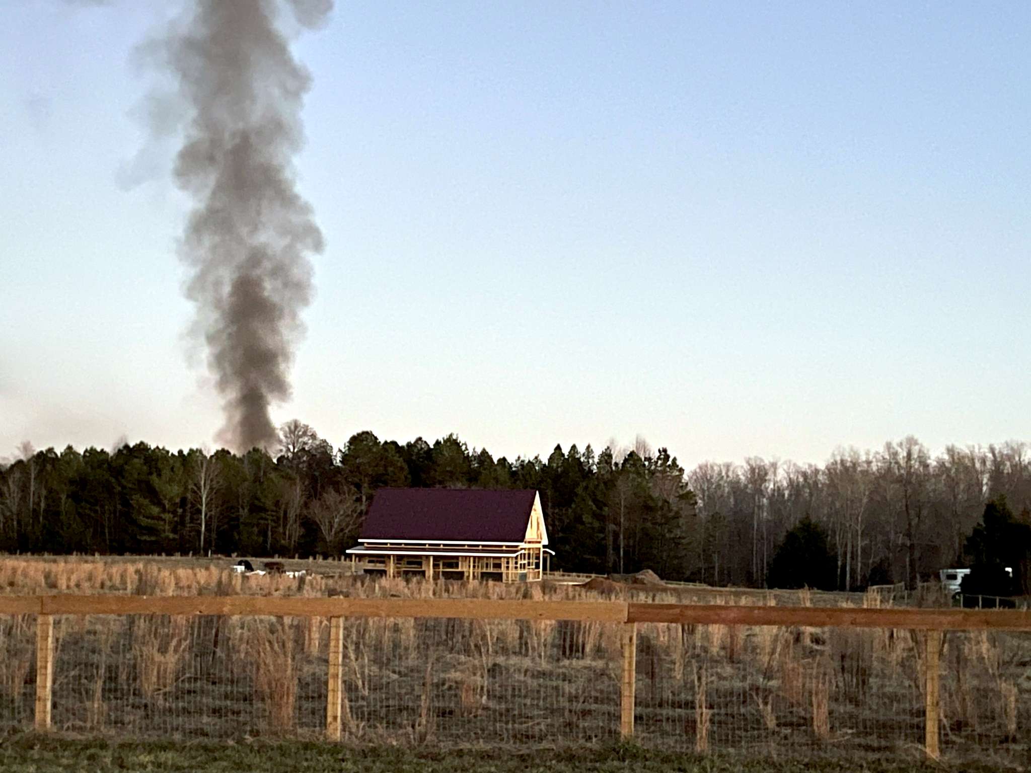 A large plume of smoke coming up out of trees behind a barn
