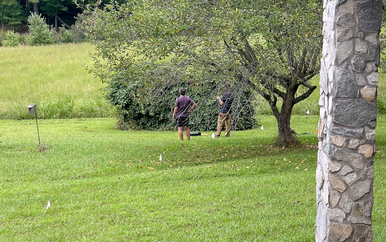Andrea and Michael looking at the proposed panel location with flags marking the trench and Michael flying a drone