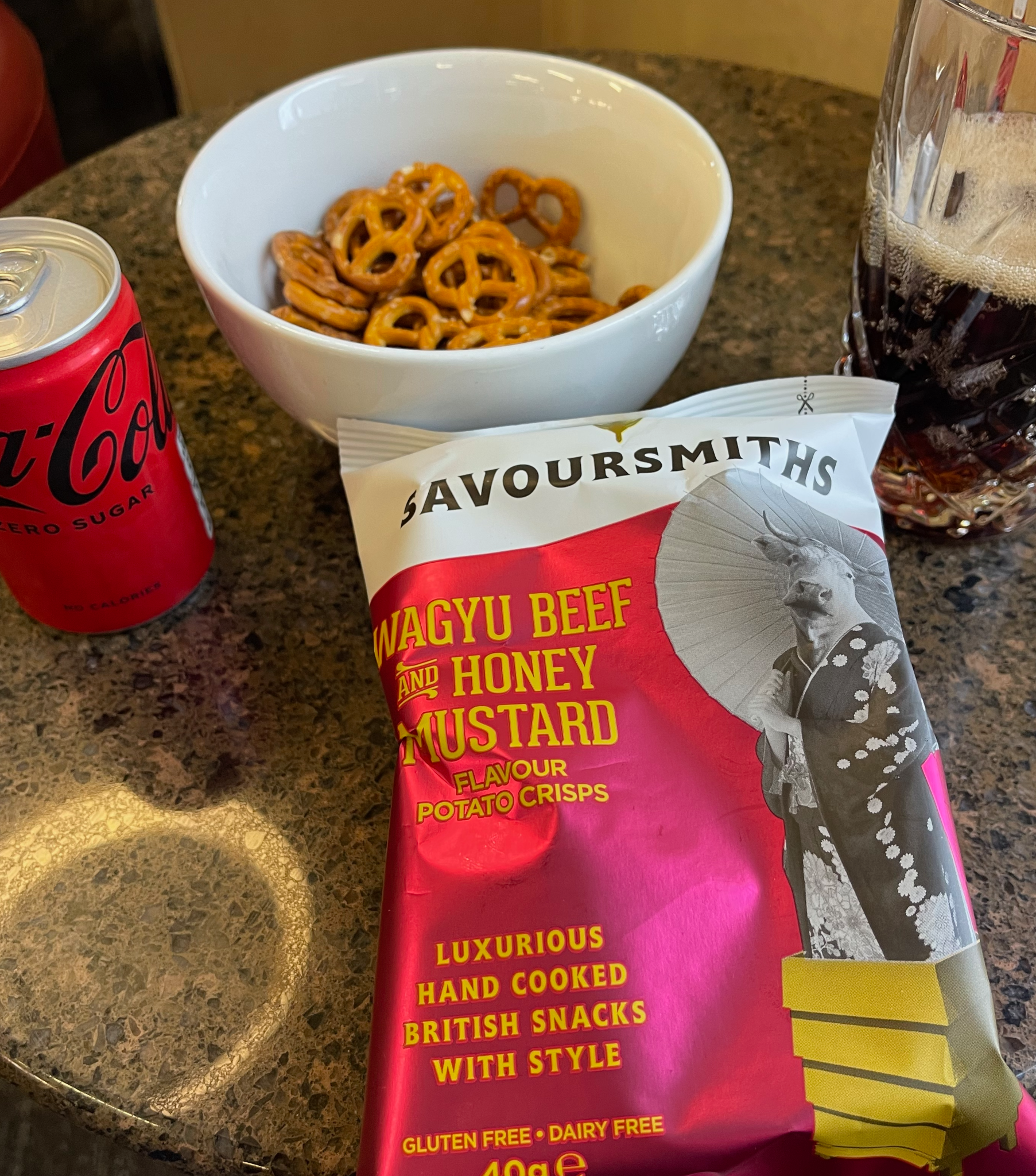 A table with pretzels, a drink and a packet of crisps